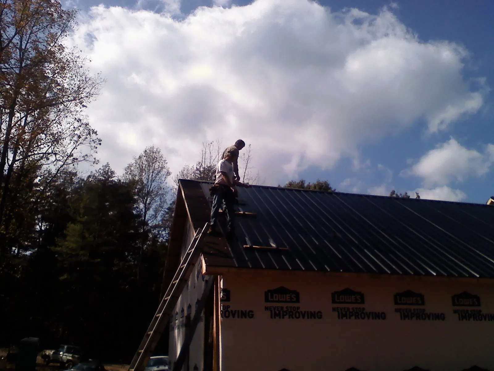Roofer fastening dark metal panels high against a cloudy sky, from a Roof Inspection job in Taylor